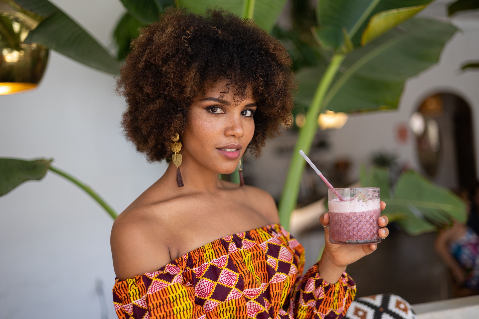 Beautiful young african woman holding a smoothie inside a modern restaurant with plants
